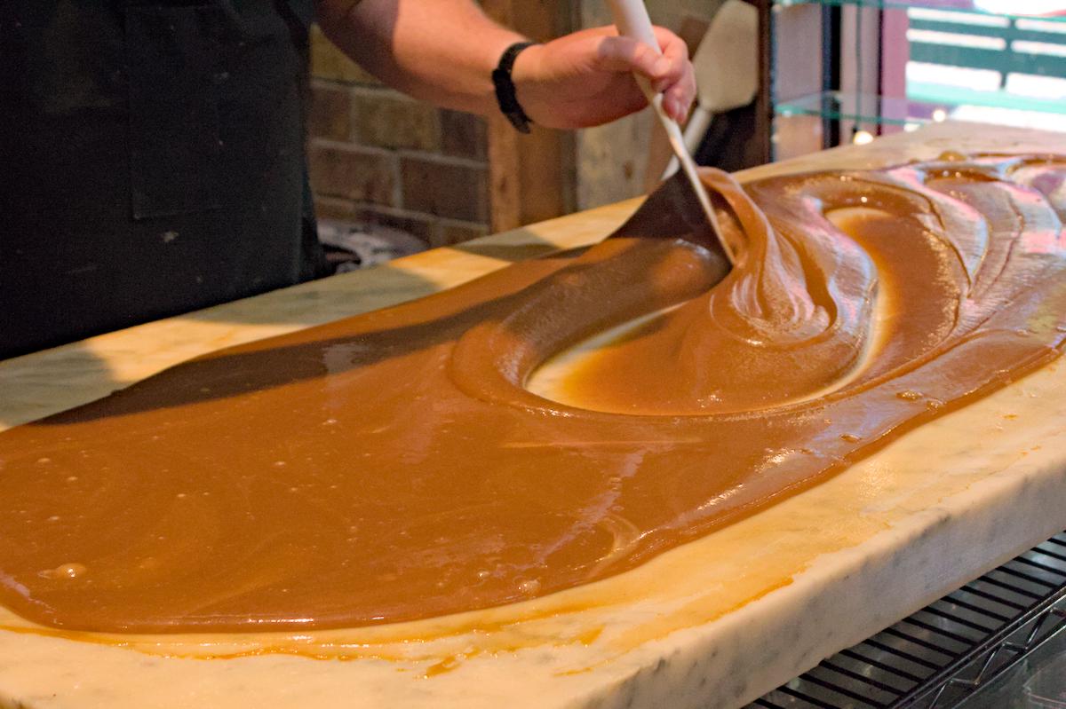 Stirring a fresh batch of handmade fudge as it cools on marble counter.
